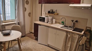 A compact kitchen with a microwave, coffee maker, and sink. There is a small refrigerator, a dining table with chairs, and a window with curtains. - Studio Apartment 'Centre Historique Beaucaire' with Wi-Fi (Beaucaire)