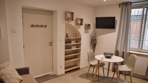A room with a door, a small table with chairs, a TV mounted on the wall, and a window with curtains. - Studio Apartment 'Centre Historique Beaucaire' with Wi-Fi (Beaucaire)