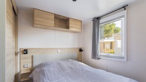 Un dormitorio con cama, cabecera de madera, ventana con cortinas y estante empotrado sobre la cama.
