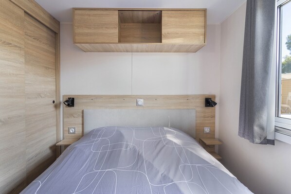 Una camera da letto con un letto, una testiera in legno, spazio contenitivo integrato, comodini e una finestra con tende.