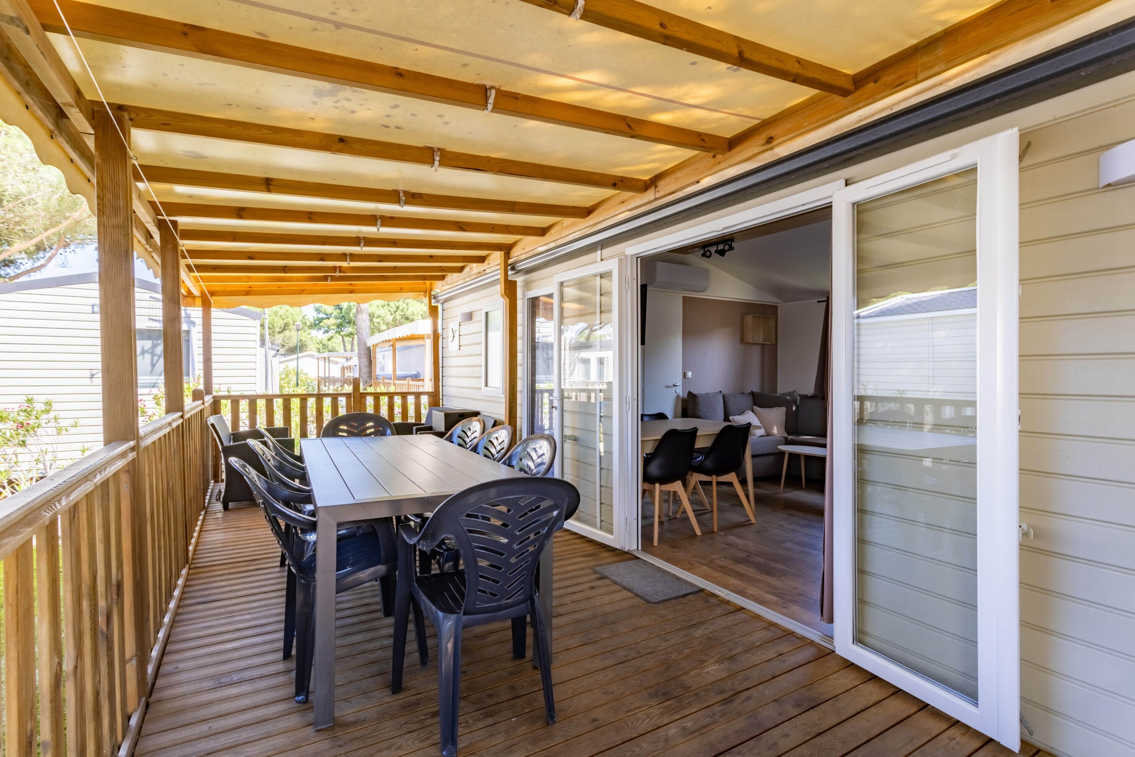Une terrasse couverte avec une table et des chaises, une terrasse en bois et une porte-fenêtre coulissante donnant sur un espace intérieur.