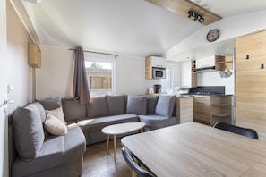 Un espace de vie compact comprenant un canapé, une table à manger, un coin cuisine et une horloge murale.