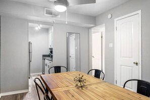 A dining area with a wooden table, four chairs, a ceiling light, and a kitchen in the background. - Arlington 2BR | AT&T, Globe Life, 6 Flags, Parking (Arlington)