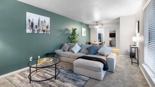 Uma sala de estar com sofá, mesa de centro e uma pintura da paisagem urbana na parede.