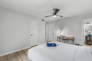Une chambre d’hôtel comprenant un lit, un bureau, une chaise, un ventilateur de plafond et une salle de bain avec un lavabo et un miroir.