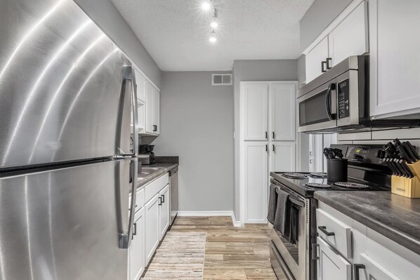 A modern kitchen with stainless steel appliances, white cabinetry, and a wooden floor.