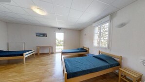 Ein Schlafraum mit drei Holzbett, einem kleinen Tisch und einem Fenster.