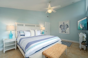 A bedroom with a bed, two bedside tables, a ceiling fan, a door, a framed artwork, a television, and a small white cabinet with an orchid plant. - Green Turtle Oasis: 4BR Canal Front Home, Pool, Dockage, Outdoor Dining & Pets (Sugarloaf Key)