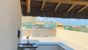 A covered outdoor area with a sink, a hand sanitizer dispenser, and a view of a building with a yellow roof in the background. - Your complete studio apartment in Porto de Galinhas, sun and sea! (Ipojuca)