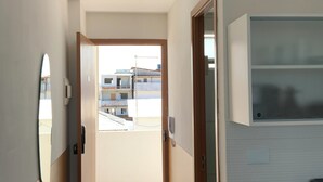 A hallway with a door leading to a balcony, a small kitchen area, and a mounted air conditioning unit. - Your complete studio apartment in Porto de Galinhas, sun and sea! (Ipojuca)