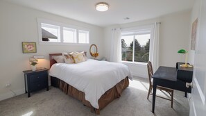 Un dormitorio con cama, mesitas de noche, escritorio, silla, ventana y vista al exterior.