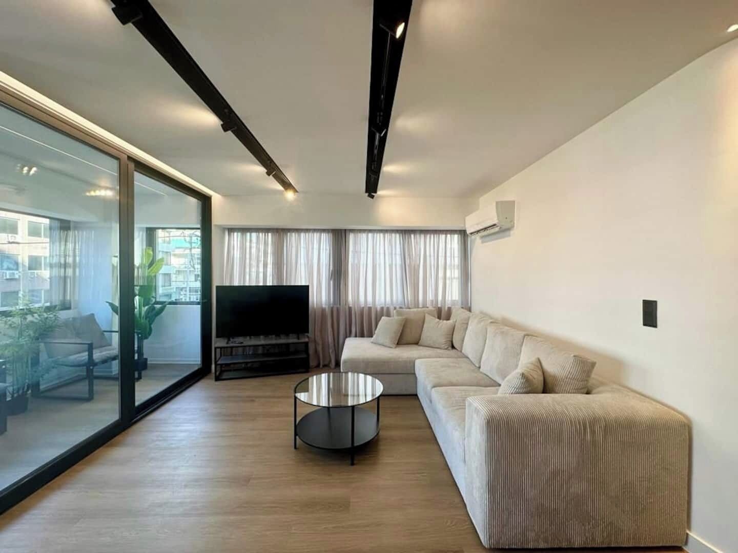 A modern living room with a large window, a sofa, a coffee table, and a flat-screen TV.