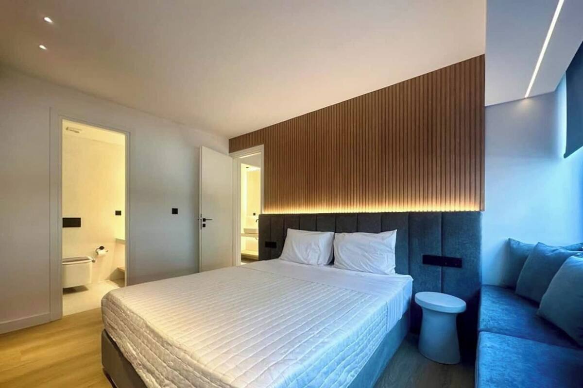 Une chambre d’hôtel moderne avec un grand lit, une table de chevet, une petite commode ronde et un canapé.