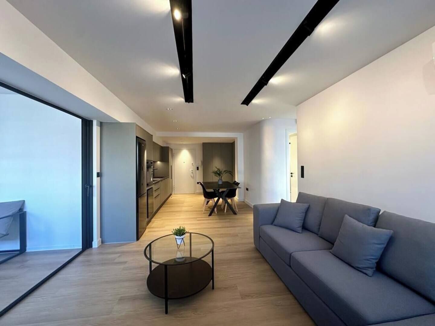 A modern living room with a sofa, a coffee table, and a dining area in the background.