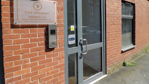 A brick building with a glass door, a security intercom, and a sign indicating 'The Foundry Apartments 14-45.'
