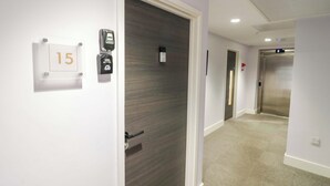 A hallway with a door marked '15', a wall-mounted intercom, and an elevator.