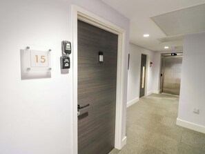 Een gang met een deur met het nummer '15', een intercom aan de muur en een lift.