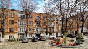 A courtyard with a cobblestone ground, parked cars, and a bench surrounded by potted plants. - Cozy 1-bedroom apartment in the City Center in București (București)