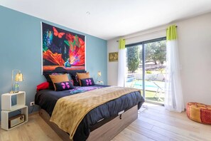 Une chambre avec un lit, un grand tableau, une fenêtre avec des rideaux et une vue sur une piscine.