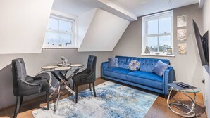 Een modern loft appartement met een schuine plafond, een blauwe bank, twee zwarte stoelen, een kleine ronde tafel en een aan de muur bevestigde televisie.