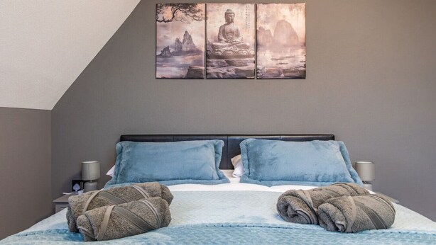 Een slaapkamer met een bed, twee kussens, een dekbed en een wanddecoratie.