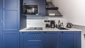 Een kleine keuken met blauwe kastjes, een inbouwoven, een koffiezetapparaat en een waterkoker.