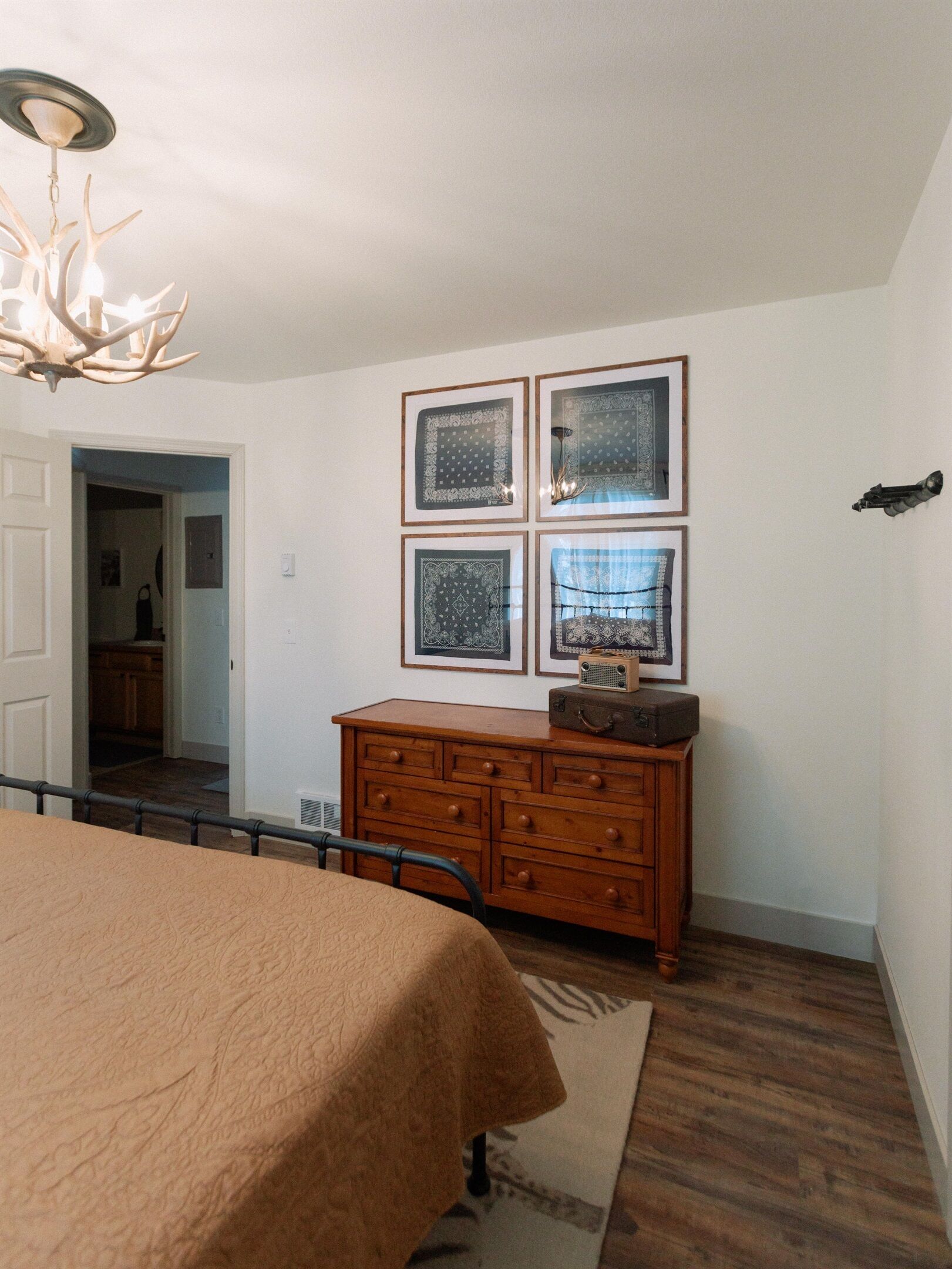A bedroom with a bed, a dresser, a chandelier, and framed pictures on the wall.