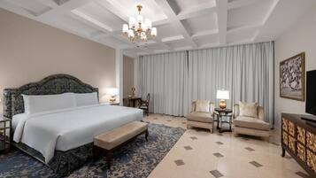A hotel room with a large bed, two armchairs, a bench, a chandelier, and a television.