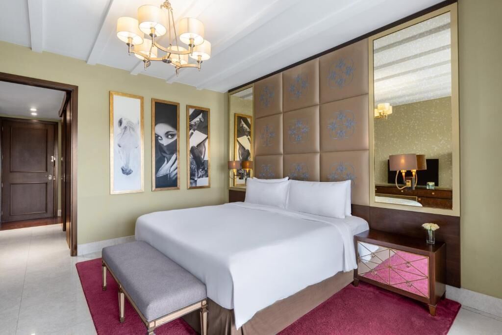 A hotel room with a large bed, a bench, a mirror, and artwork on the wall.