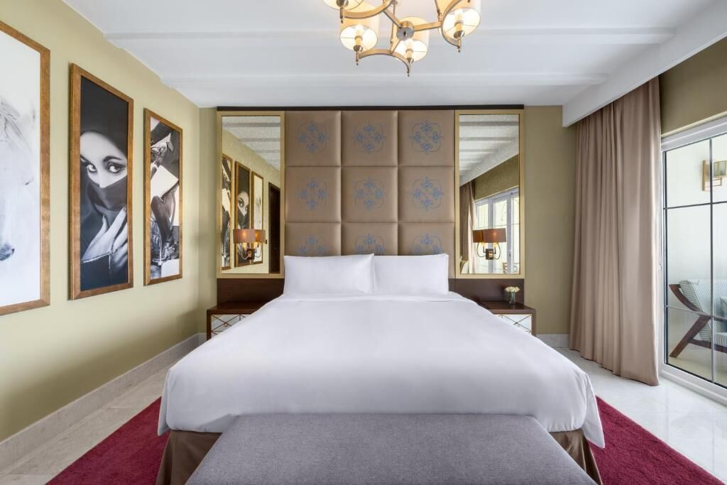 Una camera d'albergo con un letto grande, un lampadario, uno specchio e opere d'arte alle pareti.