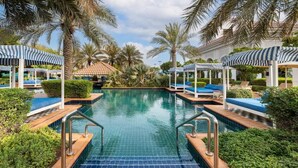 A swimming pool with lounge chairs and umbrellas, surrounded by palm trees and greenery. - The Mirage VIP At Habtoor polo Resort  (Dubai)