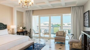 A hotel room with a large bed, a chandelier, a balcony with chairs, and a view of buildings. - The Mirage VIP At Habtoor polo Resort  (Dubai)