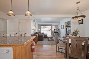 A kitchen with a wooden island, pendant lights, a dining area with a table and chairs, and a view through a window. - Alpine Escape, Cool Pool-Spa, Lakes & Trails Galore, Near Fine Dining / Bars (Mammoth Lakes)