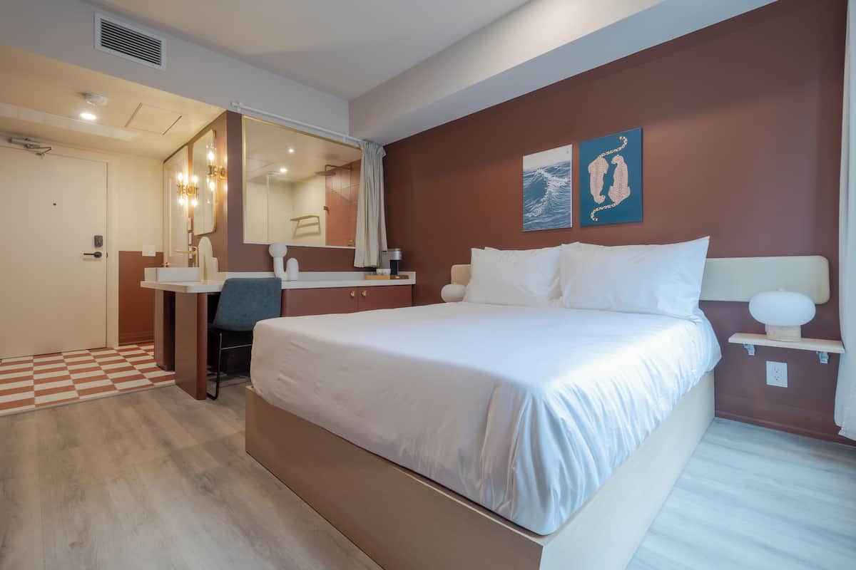 A hotel room with a bed, a desk, a mirror, and a bathroom.