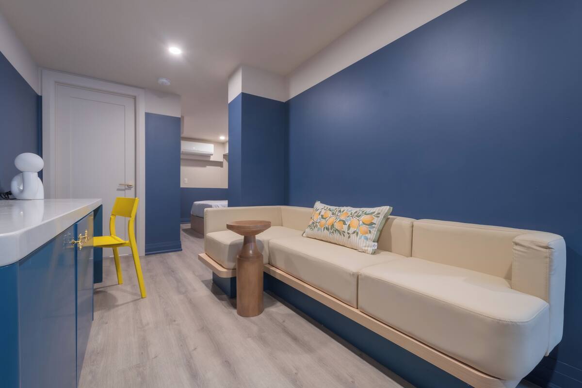 A modern living area with a sofa, a small round table, a yellow chair, and a white countertop.
