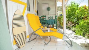Ein gelber Liegestuhl, ein Surfbrett und ein Tisch mit Stühlen auf einer gefliesten Terrasse.