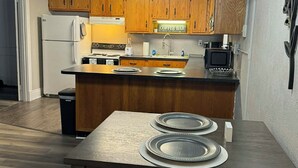 A compact kitchen with wooden cabinets, a central island, a chandelier, and a dining table with plates. - Cozy 1-bedroom apartment in charming Shepherdsville with AC (Shepherdsville)