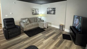 A living room with a sectional sofa, a black leather chair, a TV, and artwork on the walls. - Cozy 1-bedroom apartment in charming Shepherdsville with AC (Shepherdsville)