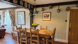 A dining area with a wooden table and chairs, a vase of yellow flowers, and a framed picture on the wall. - Countryside Farmhouse - Glasgow - Sleeps 6 (Eaglesham)
