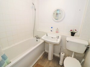 A bathroom with a bathtub, sink, toilet, and a small mirror. - Carpenters Court (Birmingham)