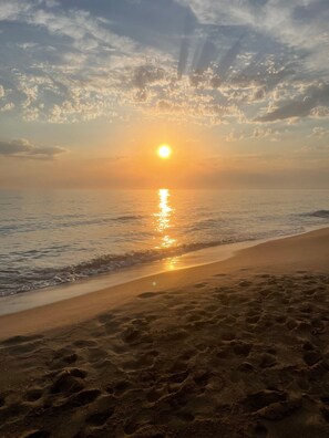 A beach with footprints leading to the water, a clear sky, and the sun setting over the horizon. - Bouganvillea Holiday Home in Sabaudia with Terrace, Wi-Fi, and Parking (Sabaudia)