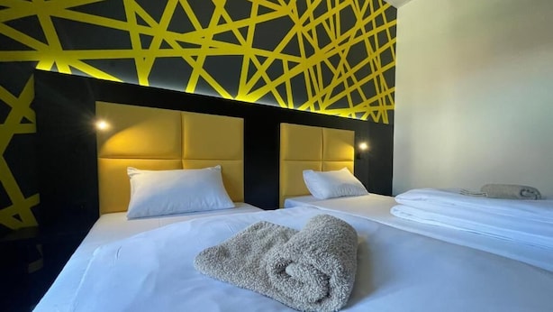 A hotel room with a bed, two bedside tables, and a geometric yellow wall design. - ONRest Hostel (Kielce)