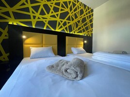 Una habitación de hotel con una cama, dos mesitas de noche y un diseño geométrico amarillo en la pared.