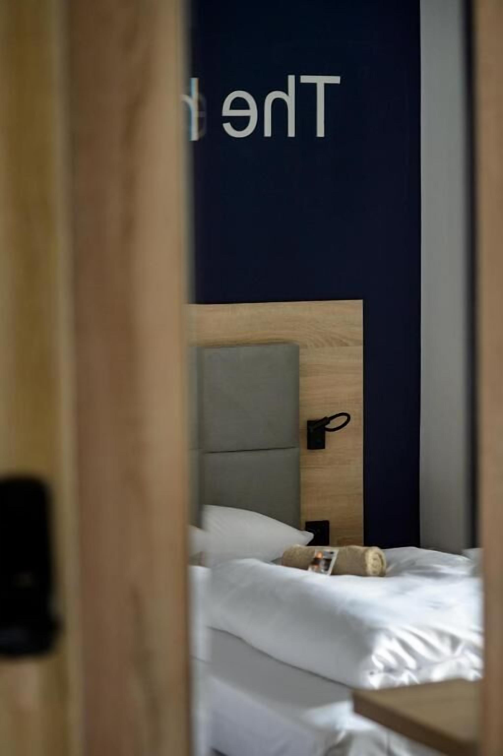 A hotel room with a wooden headboard, a bed with white linens, and a small bedside table.