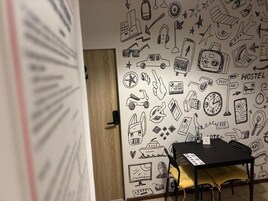 Una habitación con una pared decorada con diversos garabatos, una mesa con una silla y una puerta al fondo.
