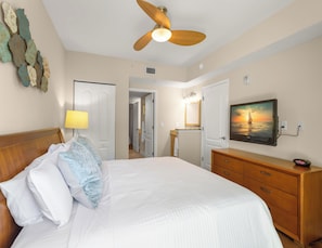 A hotel room with a bed, a wooden dresser, a television, and a ceiling fan.