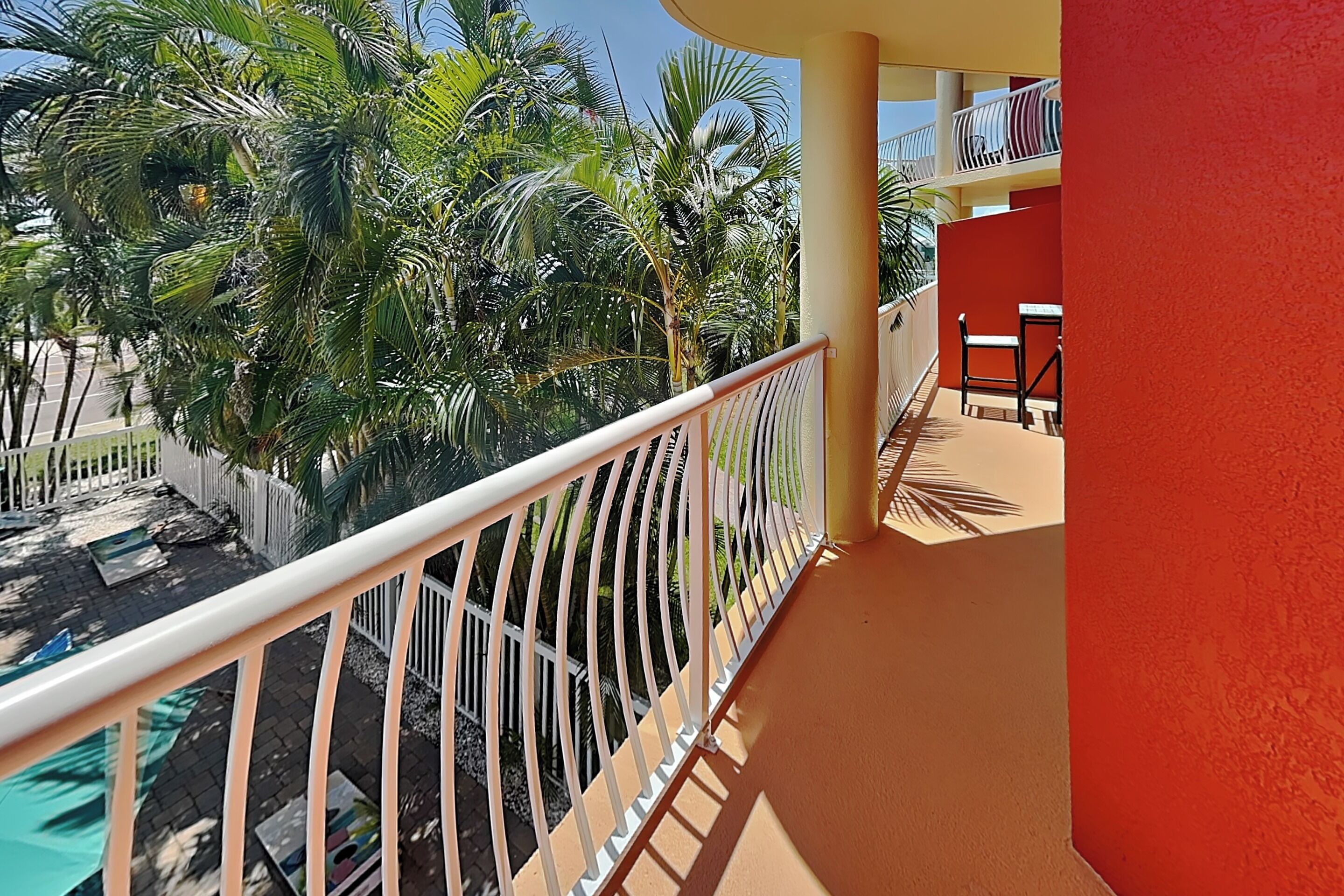 Ein Balkon mit weißer Reling, ein Pool und im Hintergrund Palmen.