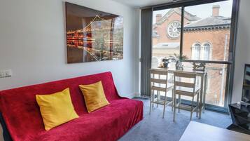 A room with a red sofa, a table, and a large window with a view of a building.