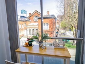 A window with a view of a red brick building, a clock, and a table with a plant and a sculpture. - Viva Apartment (Birmingham)