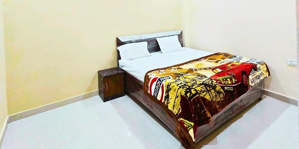 A single bed with a patterned bedspread, a wooden nightstand, and a white wall.